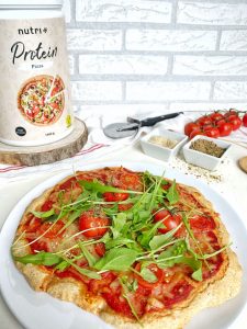 Pizzateig mit Tomaten und Rucola belegt
