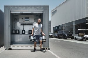 Mann trägt zwei Fäässer aus Metall von einer Station