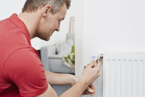 Mann schaut sich ein Thermostat an der Heizung an